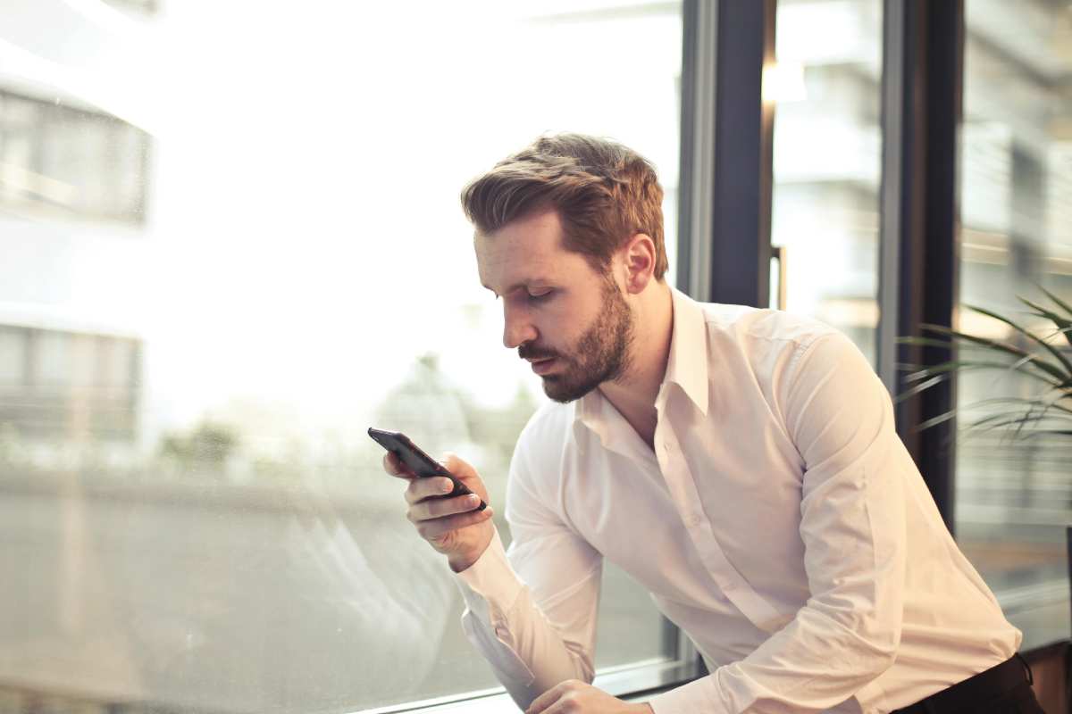 Un ragazzo con una camicia bianca legge un messaggio sul telefono