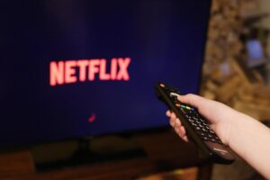 Telecomando in mano direzionato verso una tv sintonizzata su Netflix
