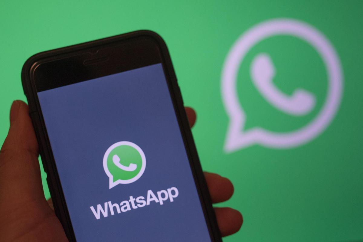 Cellulare tenuto in mano su schermata d'apertura WhatsApp, sullo sfondo logo WhatsApp