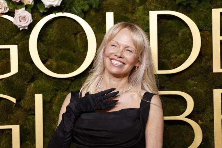 Pamela Anderson sorride e si porta la mano sul collo