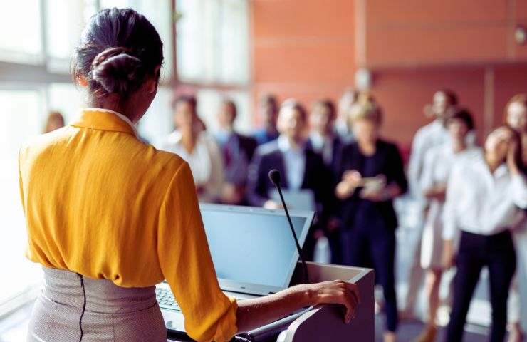 persone ascoltano una donna che parla al microfono